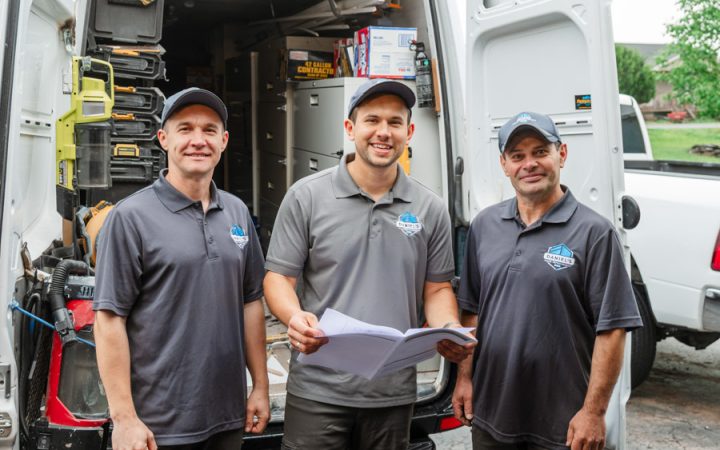 Three members of the Daniel's Home Improvement team standing in front of their work van, reviewing project plans.