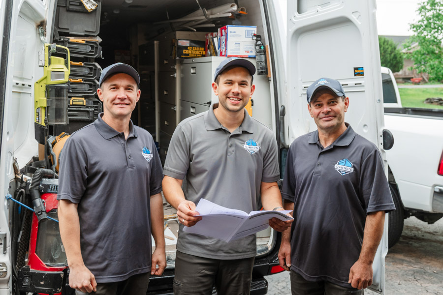 Three members of the Daniel's Home Improvement team standing in front of their work van, reviewing project plans.