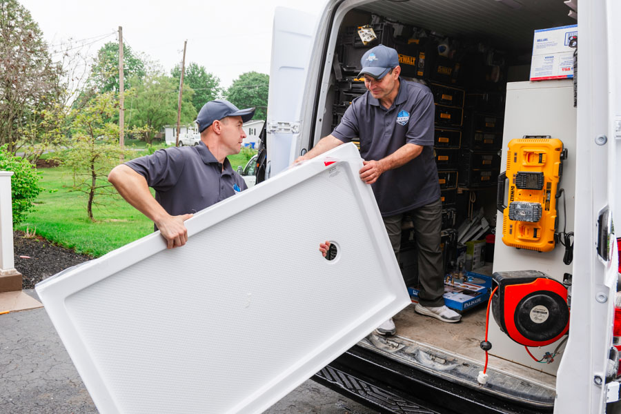Two professionals from Daniel's Home Improvement unloading a large white panel from their work van.