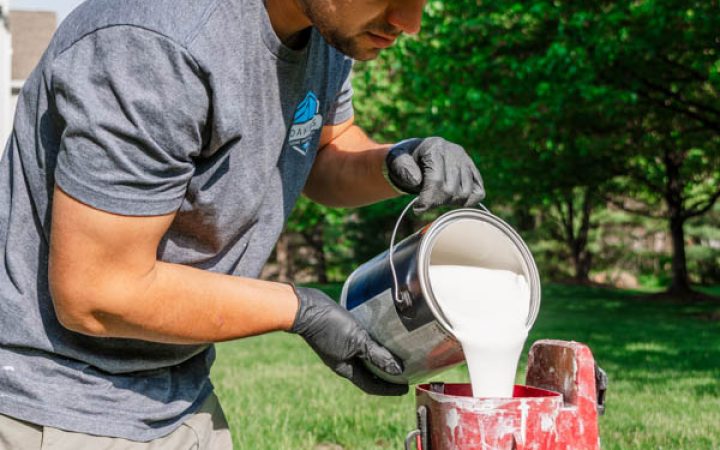 A member of the Daniel's Home Improvement team pouring paint into a sprayer for an outdoor painting task.