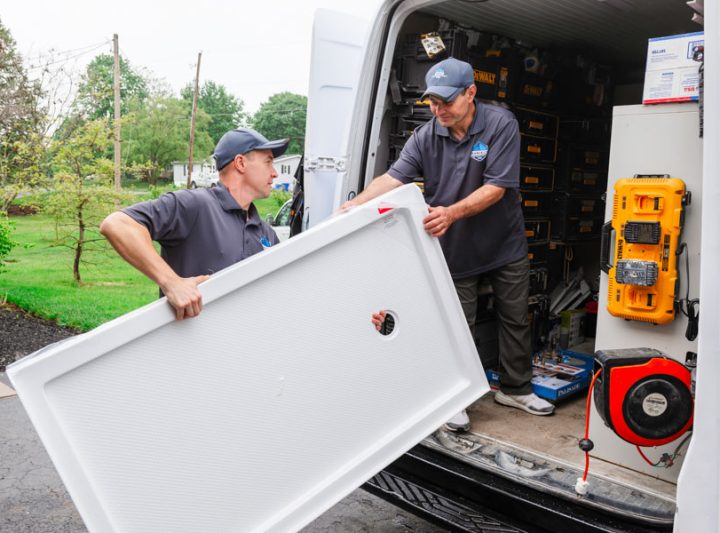 Two professionals from Daniel's Home Improvement unloading a large white panel from their work van.