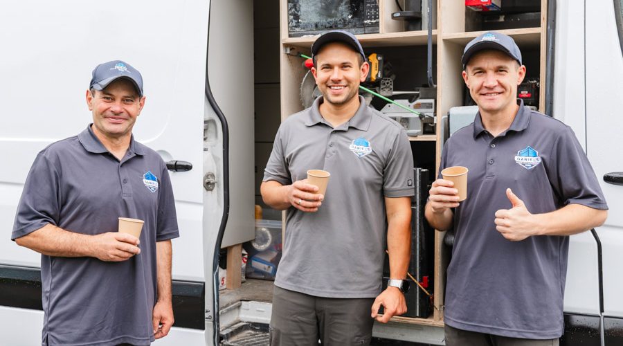 The Daniel's Home Improvement crew standing together, holding coffee cups and giving thumbs up, showcasing teamwork and readiness for the day’s tasks.